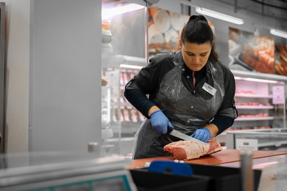 Metzgerin schneidet ein Stück rotes Fleisch auf einem roten Schneidebrett in einer Metzgerei.