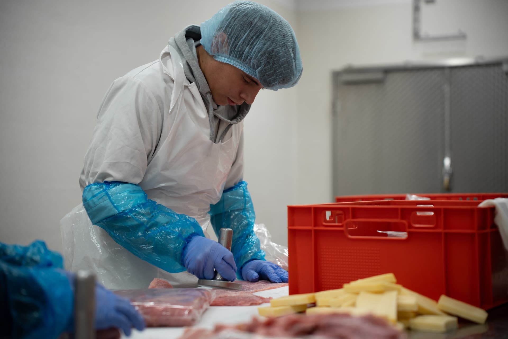 Ein Mitarbeiter schneidet Fleisch mit Schutzhandschuhen.